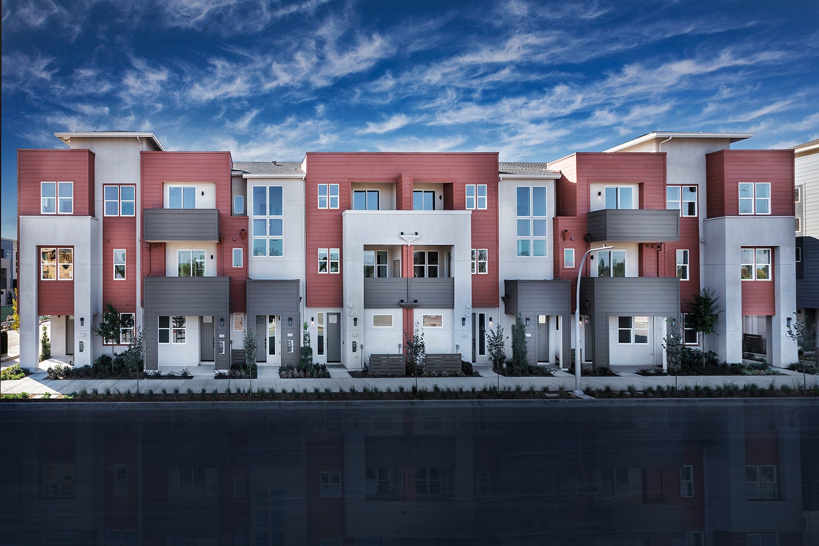 Modern apartment complex at dusk, with sleek lines and large windows. Warm interior lights contrast with a vivid purple and orange sunset sky.